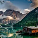 mirror lake reflecting wooden house in middle of lake overlooking mountain ranges