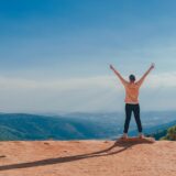 person in beige top on mountain cliff